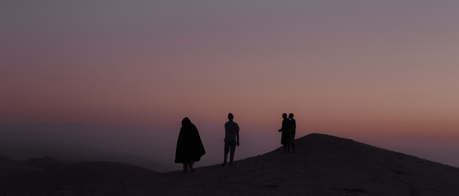 Four silhouettes on dune ridge at twilight